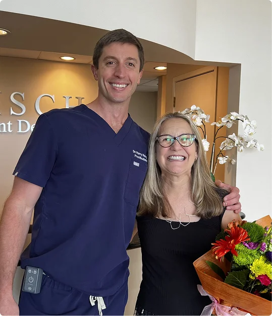 Dr. Harry Misch, a specialist prosthodontist, smiling with a happy patient holding flowers at Misch Implant Dentistry.